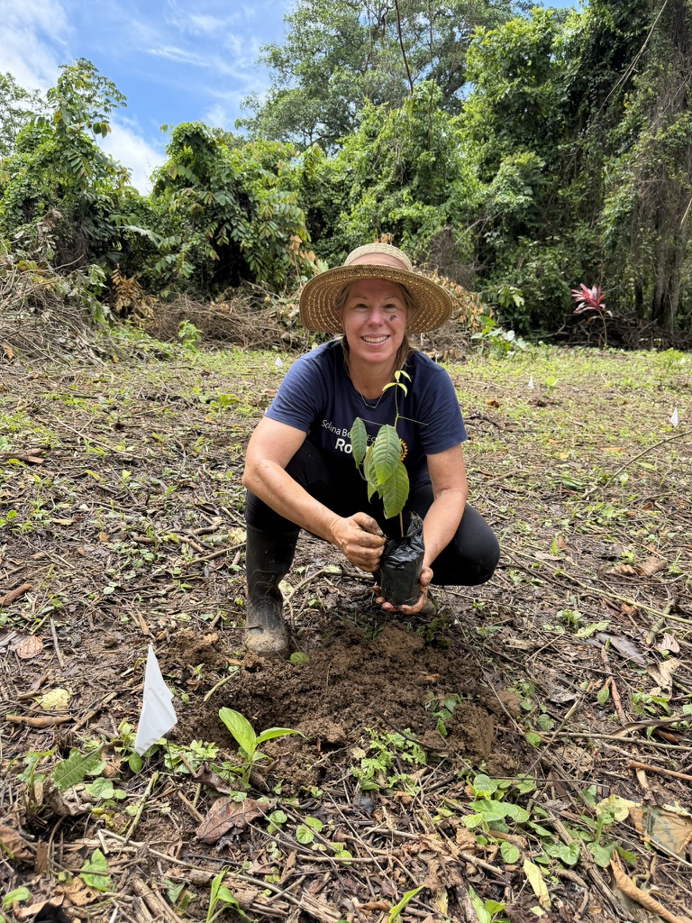 Alisa Morrison in a straw hat kneeling to plant a seedling