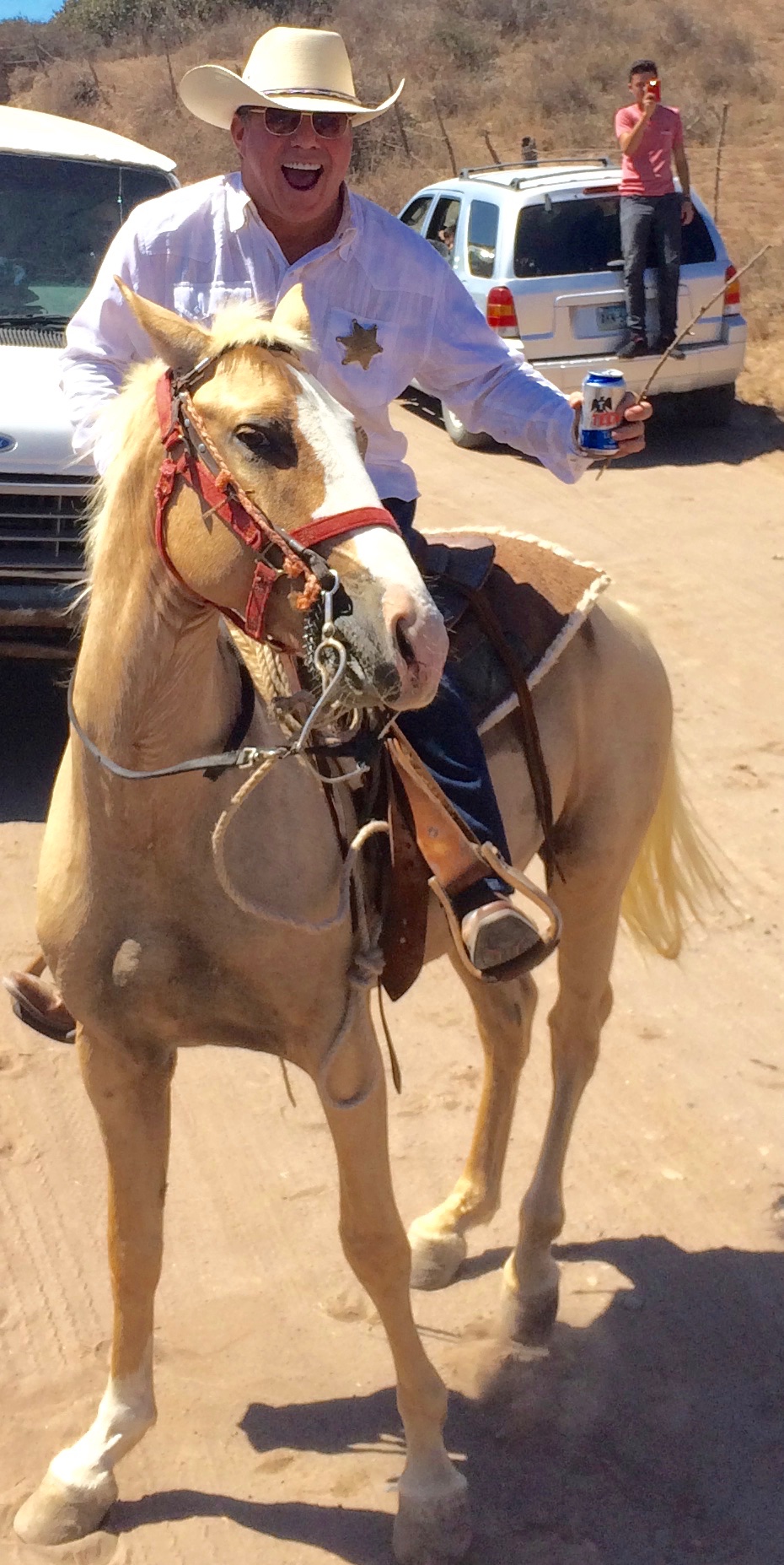 Steve Bender laughing on a palomino horse, wearing a white shirt, cowboy hat and sheriff's star
